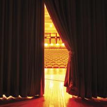 photograph of hand pulling back curtain on theater stage