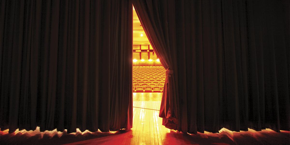 photograph of hand pulling back curtain on theater stage